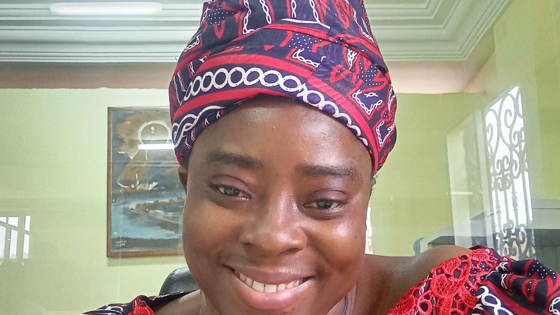I am smiling, have a headscarf and wearing one of the many traditional designs from the Grassfields of Cameroon, in a mix colour of red, balc and white.
