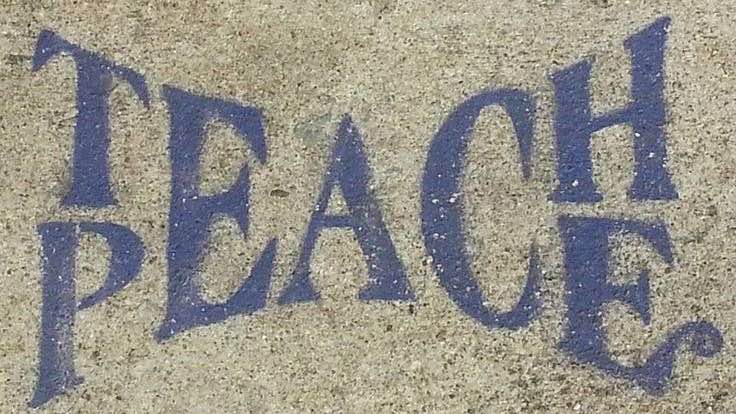 A phrase in blue saying “Teach Peace” stamped on the street
