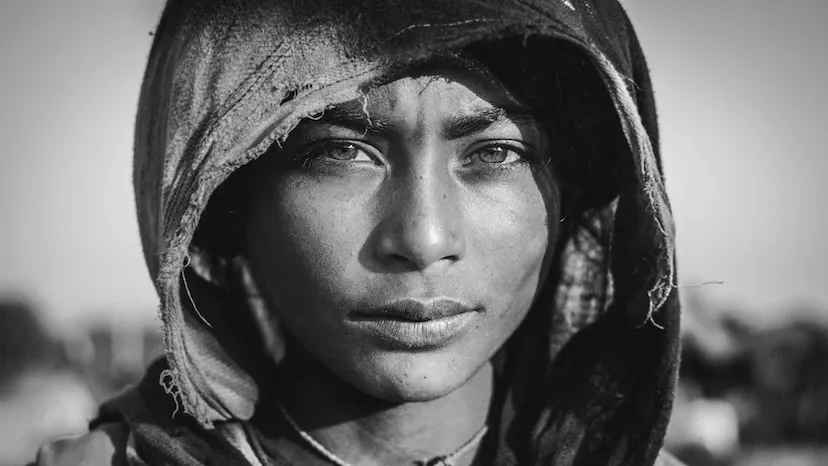 In this black and white image, a women looks into the camera with a hood covering her head.