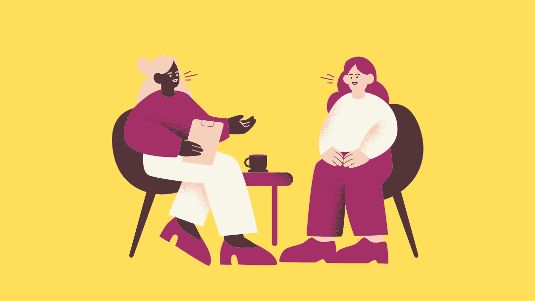 A mentor and mentee (two women) seated and having a conversation with each other.  The Mentor listens to her mentee with her accomplishment and challenges.