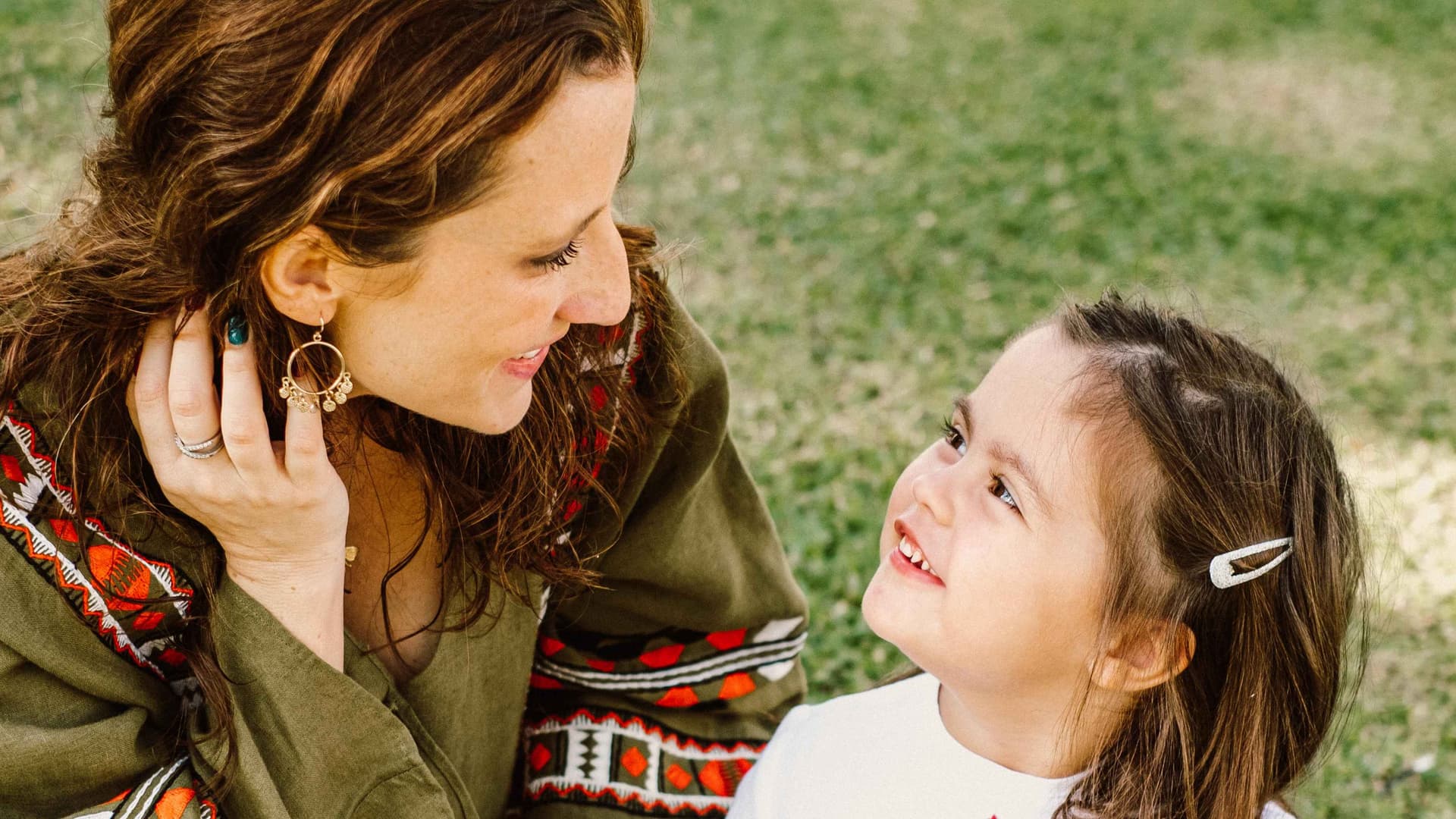 A mother and child look at each other whilst sitting on the grass