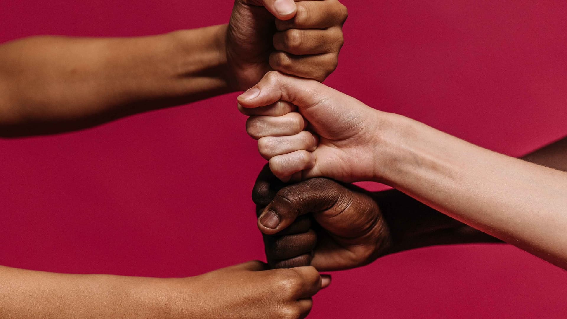 Fists of people of different cultures and race on top of eachother on a red background