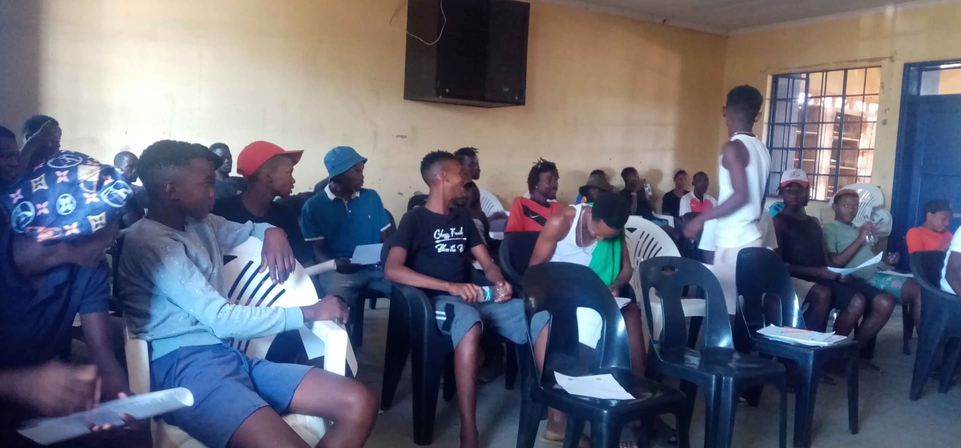Men seated closely together in a small room, their faces are pixedlated to ensure anomity, Some are leaning forward, others with heads bowed. A deep, emotional conversation about healing and masculinity