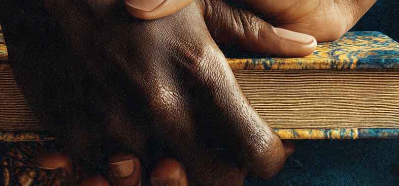 deux mains posées l'une sur l'autre, sur fond de tissus africains aux motifs dorés et bleus, symbolisant la solidarité et le soutien mutuel entre femmes.