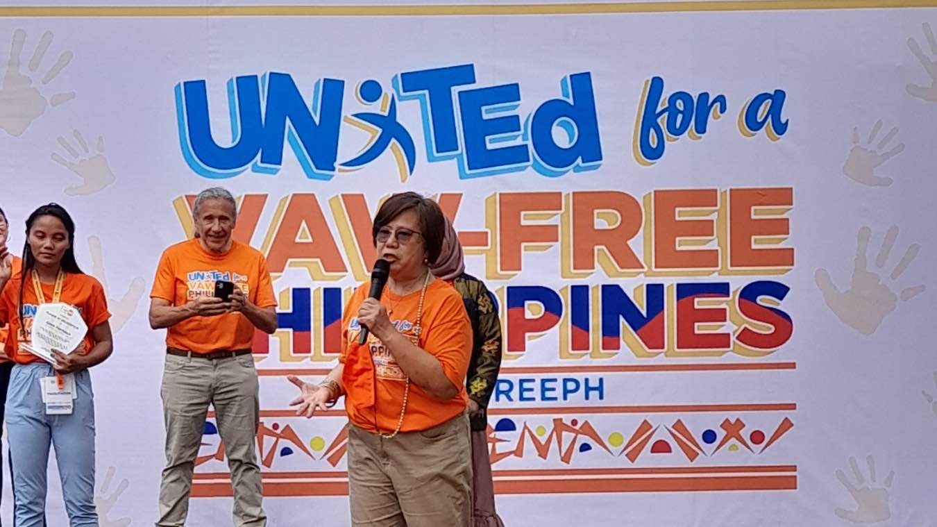 Three (3) people are on stage. 2 females and 1 male. Behind them is the stage back drop written with United for a VAW - Free Philippines
