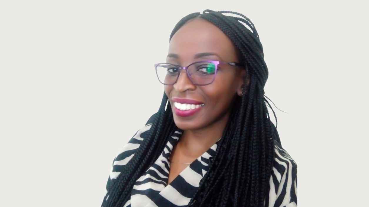 Smiling woman with braided hair and glasses, wearing a black and white striped top, against a plain background. The mood is cheerful and confident.